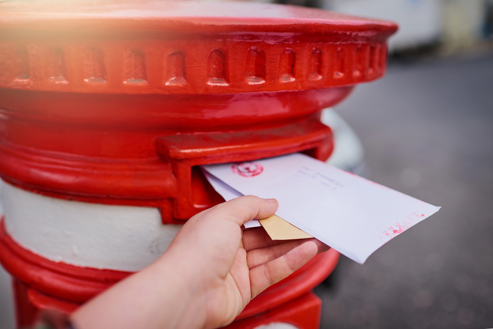 close up of hand delivering letters into a post box