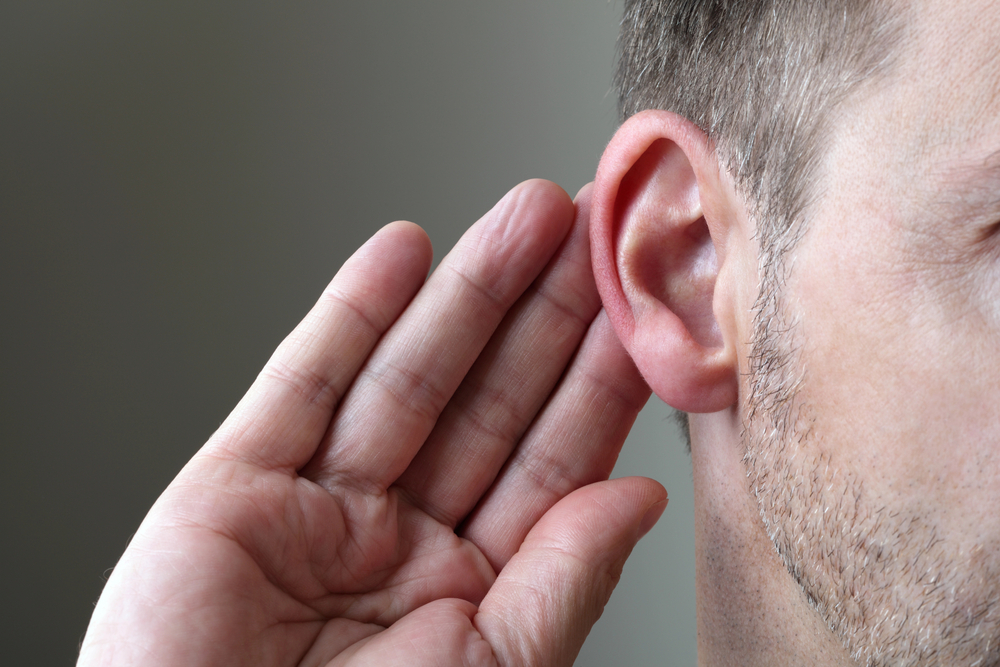 Close-up of a person leaning in attentively with their hand to their ear, indicating active listening